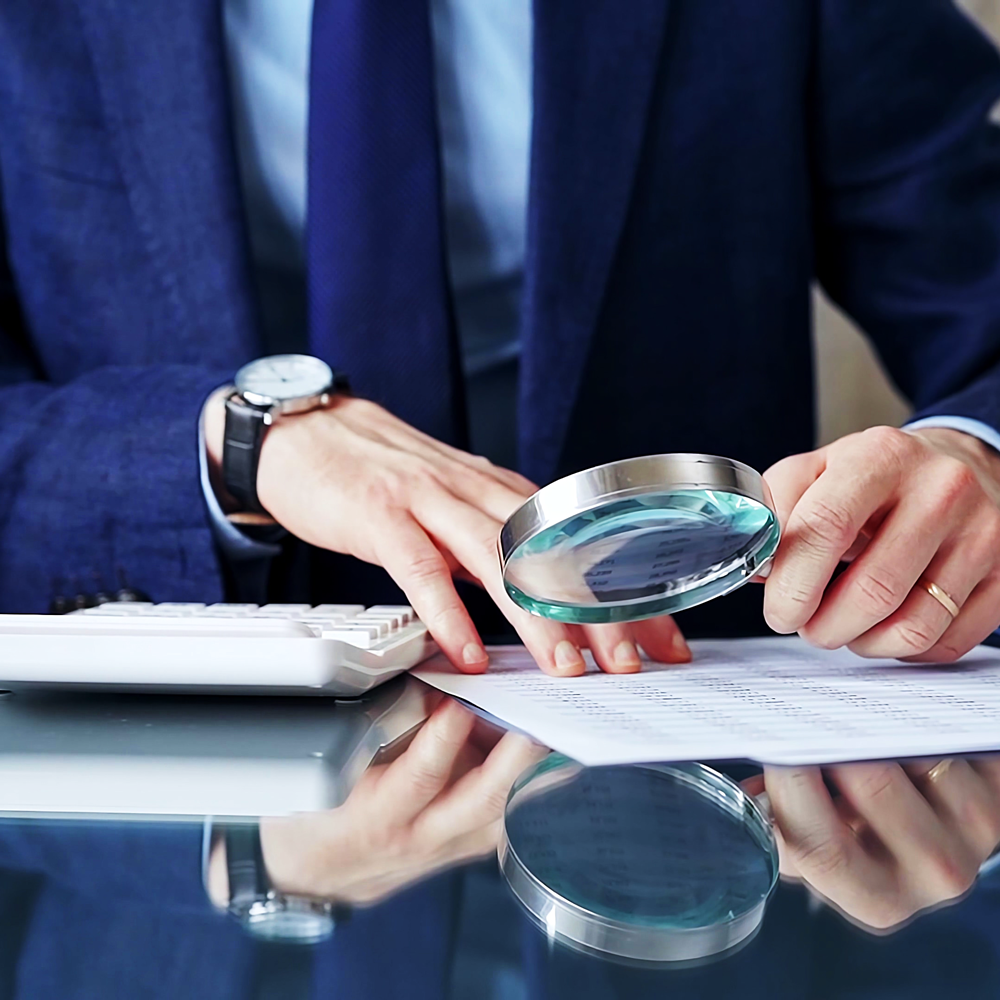 https://km-consultation.com/wp-content/uploads/2024/10/auditor-man-analyzing-financial-documents-with-magnifying-glass-calculator-his-glass-office-desk-formal-blue-jacket-business-people-concept.png